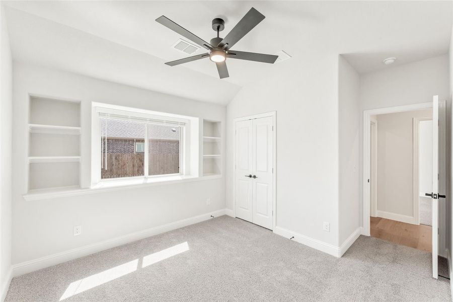 Empty bedroom with vaulted ceiling, ceiling fan, built-in shelves, and carpet flooring
