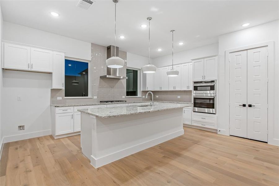 Kitchen featuring tasteful backsplash, white cabinets, a kitchen island with sink, light wood-style floors, and recessed lighting Kitchen featuring tasteful backsplash, white cabinets, a kitchen island with sink, light wood-style floors, and recessed lighting