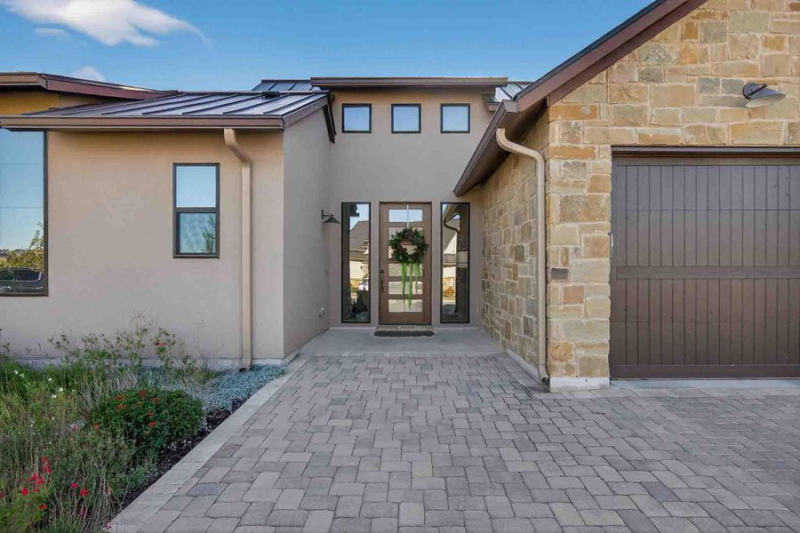 Entrance to property featuring stone siding, stucco siding, a standing seam roof, a metal roof, and an attached garage