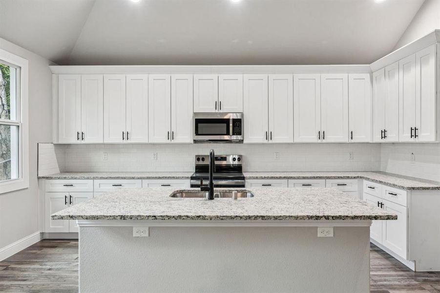 Kitchen with vaulted ceiling, granite counter top, stainless steel appliances, dark wood finished floors, and tasteful backsplash