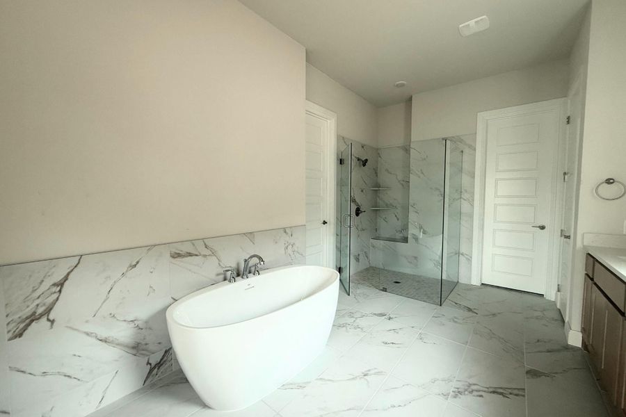 Freestanding soaking tub with chrome fixtures, set against a marble-look tiled wall Freestanding soaking tub with chrome fixtures, set against a marble-look tiled wall