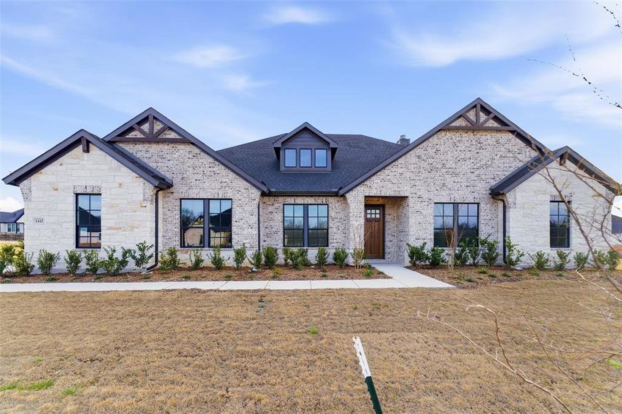 French country inspired facade featuring a front lawn, brick siding, and a shingled roof
