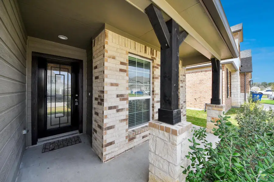 Inviting covered front porch with brick and stone columns and a stylish front entry door.