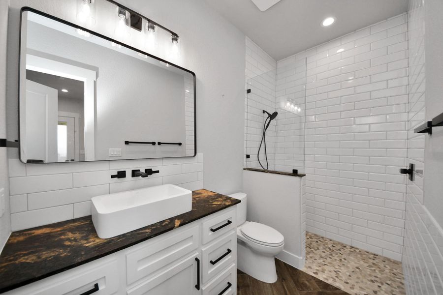 Stylish bathroom featuring a modern vanity with a vessel sink, black fixtures, and a spacious walk-in shower with sleek white subway tiles.