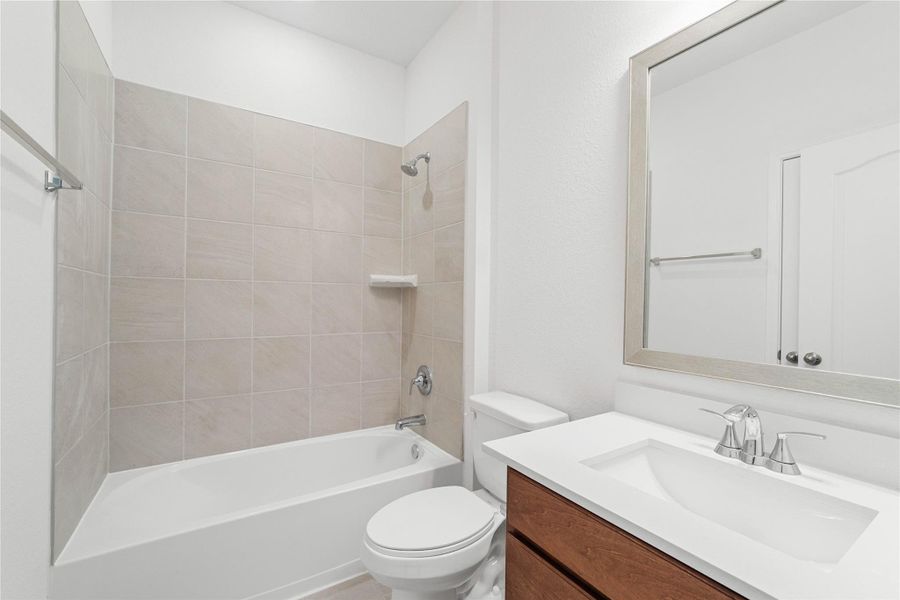 The secondary bathroom offers tile flooring, a bath/shower combination with a stylish tile surround, rich stained wood cabinetry, elegant light countertops, a framed mirror, and sleek fixtures with modern finishes. The secondary bathroom offers tile flooring, a bath/shower combination with a stylish tile surround, rich stained wood cabinetry, elegant light countertops, a framed mirror, and sleek fixtures with modern finishes.