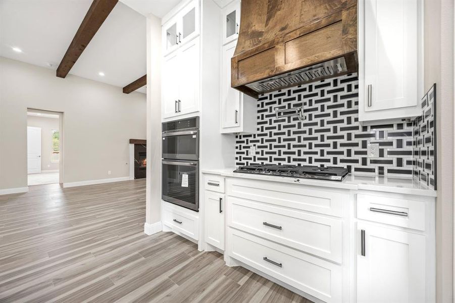 Kitchen with appliances with stainless steel finishes, custom range hood, decorative backsplash, and a pot filler on top of stove