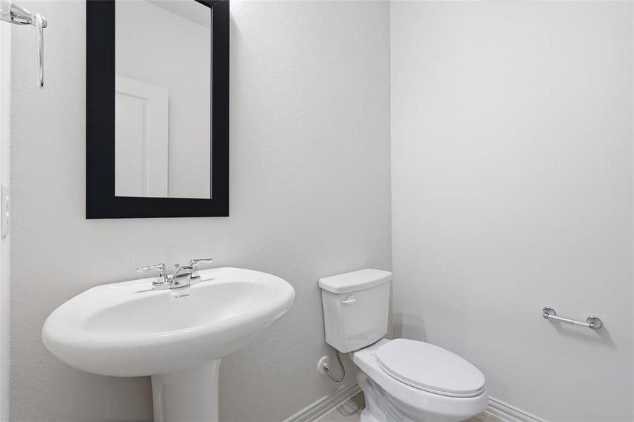 Pedestal sink with chrome faucet, complemented by a rectangular framed mirror and a modern toilet