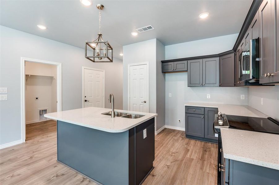 Kitchen with light hardwood / wood-style flooring, electric range oven, sink, hanging light fixtures, and a kitchen island with sink