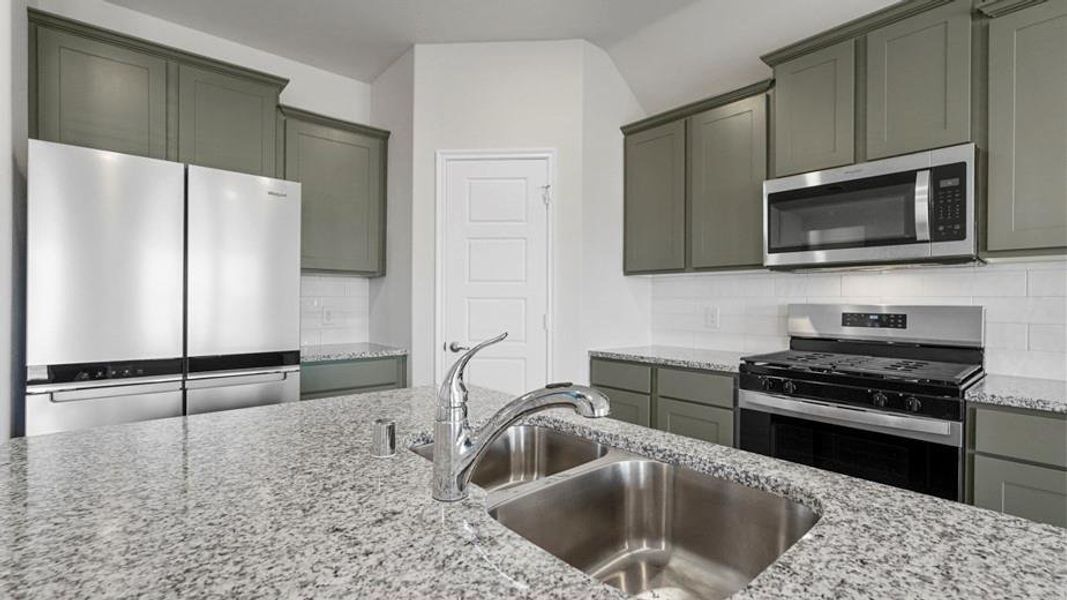 Kitchen featuring a double basin stainless steel sink, chrome faucet, granite countertops, sage cabinetry, and stainless steel appliances including a side-by-side refrigerator, microwave, and gas range Kitchen featuring a double basin stainless steel sink, chrome faucet, granite countertops, sage cabinetry, and stainless steel appliances including a side-by-side refrigerator, microwave, and gas range