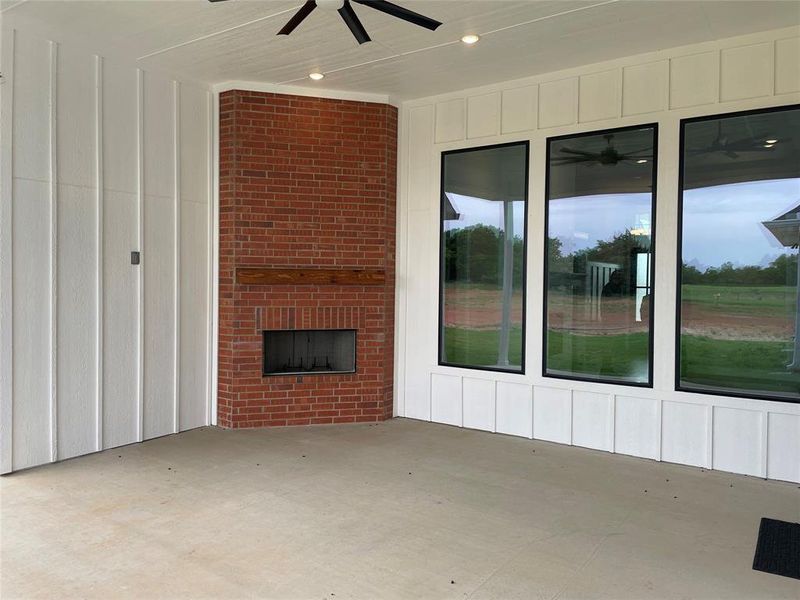 The covered patio features a brick fireplace with a wood mantel, large windows, and a ceiling fan