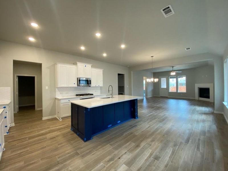 Open-concept kitchen featuring a large island with a sink, stainless steel microwave, white shaker cabinetry, and light wood-finish flooring Open-concept kitchen featuring a large island with a sink, stainless steel microwave, white shaker cabinetry, and light wood-finish flooring