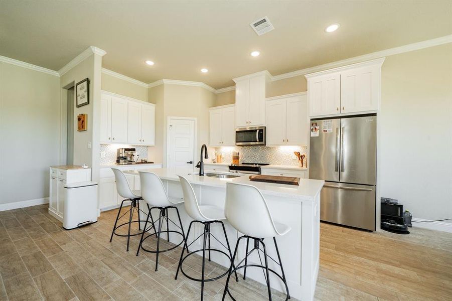 Kitchen with stainless steel appliances, a kitchen breakfast bar, white cabinetry, crown molding, and backsplash Kitchen with stainless steel appliances, a kitchen breakfast bar, white cabinetry, crown molding, and backsplash