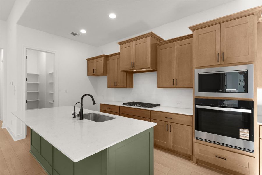 Dual tone kitchen featuring stainless steel appliances, two tone cabinetry, light stone countertops, a center island with sink, and light wood-style flooring
