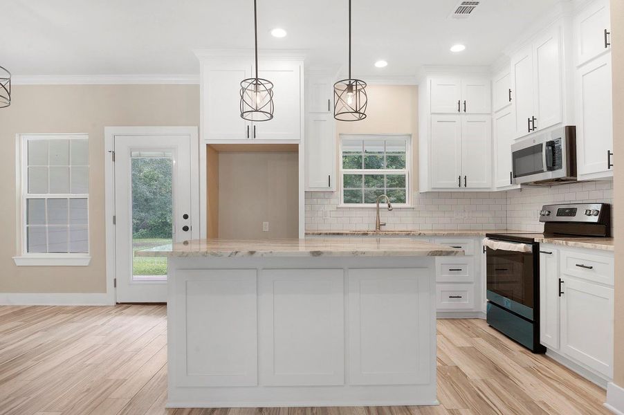 This modern kitchen features white cabinetry, a spacious marble island, and stainless steel appliances. It has a bright, open layout with natural light streaming through large windows and a glass door leading to the backyard. Perfect for cooking and entertaining. This modern kitchen features white cabinetry, a spacious marble island, and stainless steel appliances. It has a bright, open layout with natural light streaming through large windows and a glass door leading to the backyard. Perfect for cooking and entertaining.