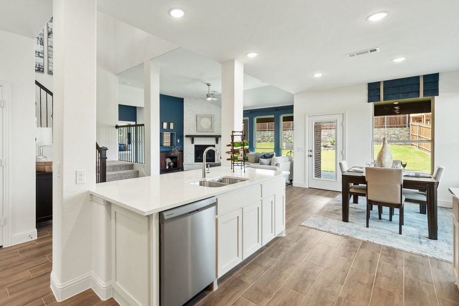 Open-concept kitchen with white island, stainless dishwasher, and views of dining and living areas with hardwood floors