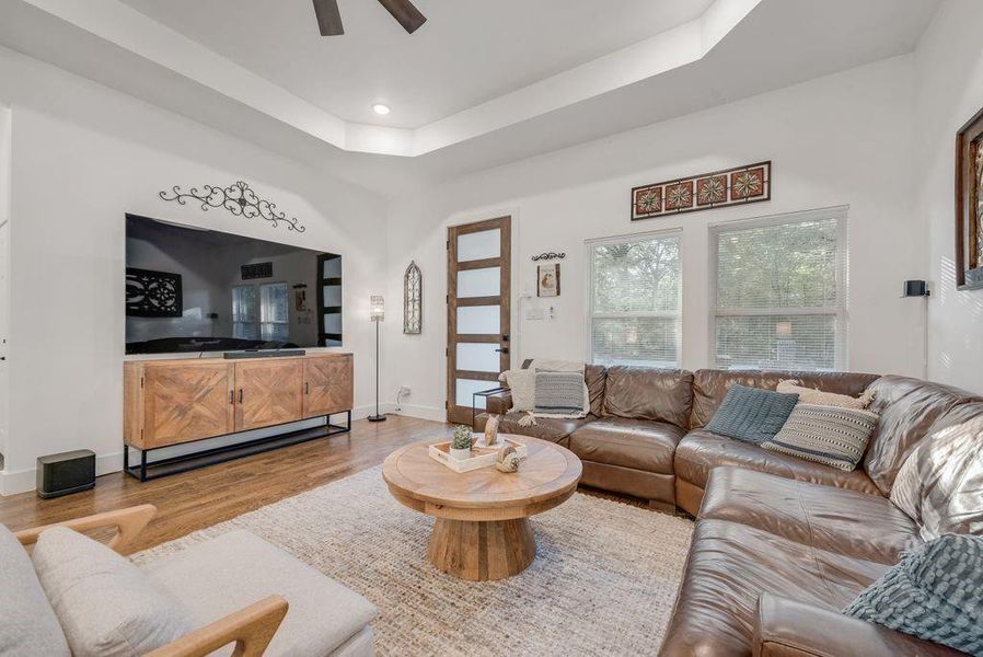 Living room featuring wood finished floors, a raised ceiling, ceiling fan, and recessed lighting
