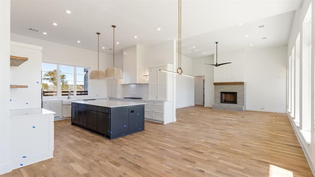 Kitchen with a center island, white cabinets, a stone fireplace, light hardwood / wood-style flooring, and decorative light fixtures