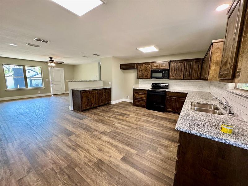 Kitchen featuring dark brown cabinets, black appliances, backsplash, dark wood-type flooring, and ceiling fan