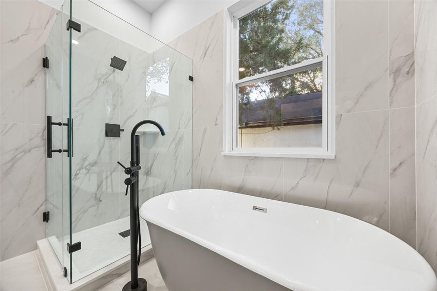 The primary modern bathroom with a freestanding tub, glass-enclosed shower, and elegant marble tile. Bright and inviting, it features a large window for natural light.