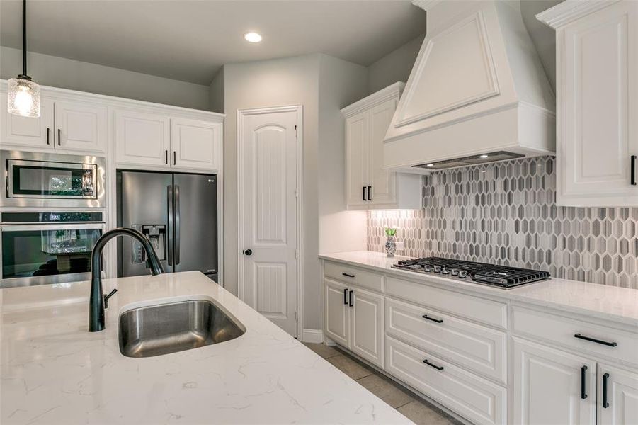 Kitchen with pendant lighting, premium range hood, backsplash, white cabinets, and appliances with stainless steel finishes