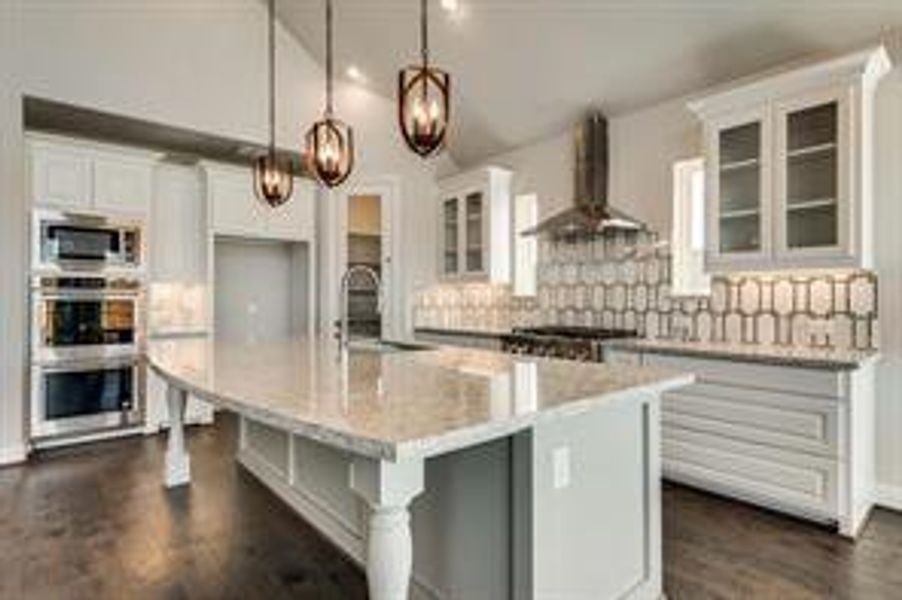 Kitchen with white cabinetry, hanging light fixtures, wall chimney range hood, a center island with sink, and appliances with stainless steel finishes