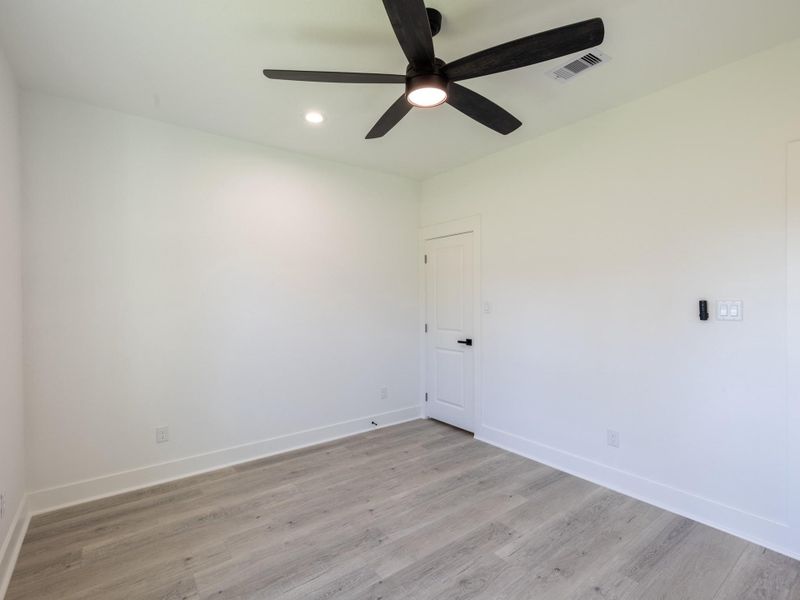 This bright room features sleek light wood flooring, a modern black ceiling fan, and fresh white walls, offering a clean and versatile space ready for personalization.