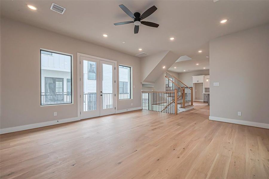 Experience modern elegance in this spacious living area, featuring light hardwood floors, neutral walls, and recessed lighting. Enjoy abundant natural light from large windows and a stylish open staircase that enhances the open-concept design.