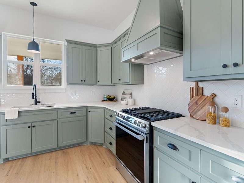 Kitchen featuring stainless steel range with gas stovetop, light wood-style floors, light stone countertops, decorative light fixtures, and decorative backsplash
