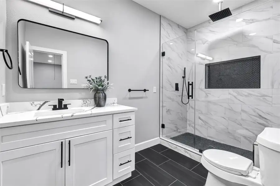 This bathroom features a sleek, modern design with a spacious glass-enclosed shower, elegant marble-style tiles, and a stylish vanity with ample storage. The monochrome color palette and contemporary fixtures create a clean, sophisticated look.
