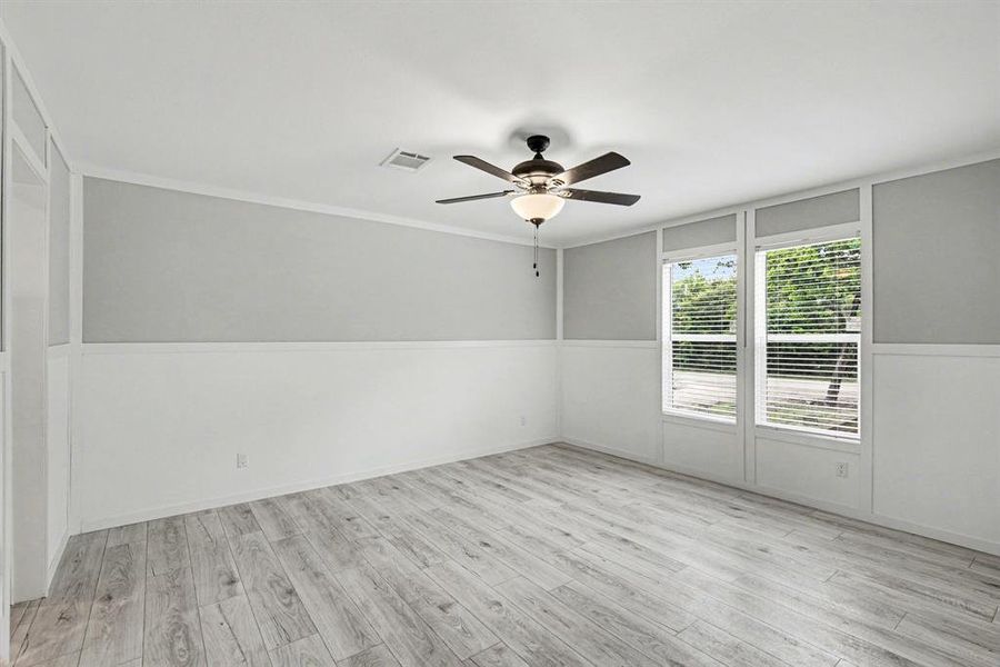Spacious primary bedroom featuring wood-finish flooring, two-tone painted walls with wainscoting, a ceiling fan with integrated lighting, and multiple windows with blinds