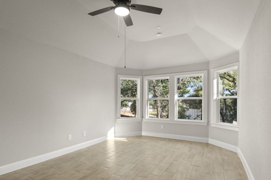 Image of a primary bedroom with light wood-like flooring and light grey painted walls, four large windows, and a black ceiling fan Image of a primary bedroom with light wood-like flooring and light grey painted walls, four large windows, and a black ceiling fan