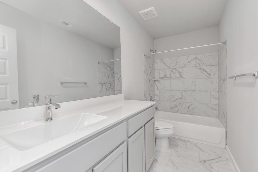 Indulge in refined charm in the secondary bathroom, where the tile flooring harmonizes with a bath/shower combo surrounded by tasteful tile. Light wood cabinets, coupled with a gorgeous countertop, elevate the space, cultivating a truly welcoming atmosphere. Sample photo of completed home with similar floor plan. Actual colors and selections may vary.
