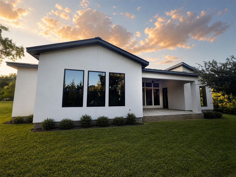 Crisp stucco walls and dark-trimmed windows define this modern exterior under a sunset sky. Crisp stucco walls and dark-trimmed windows define this modern exterior under a sunset sky.