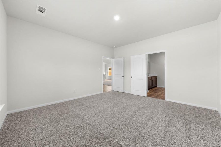 Unfurnished bedroom with carpet flooring, ensuite bath, visible vents, and baseboards