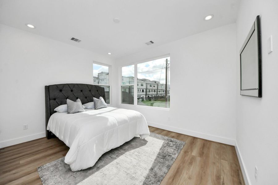 Discover the inviting second-floor bedroom, awash with natural light from expansive windows and featuring elegant wood flooring for a serene retreat.