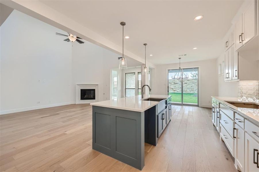 Kitchen with ceiling fan, light wood-type flooring, sink, white cabinets, and a kitchen island with sink