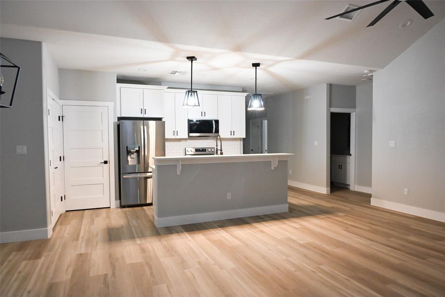 Kitchen featuring stainless steel appliances, white cabinets, light countertops, hanging light fixtures, and a kitchen island with sink