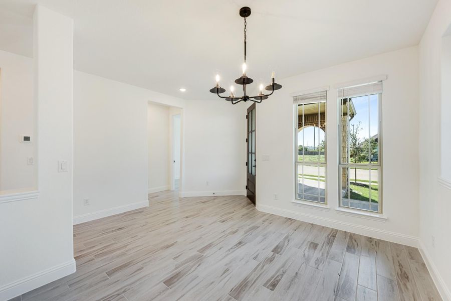 Empty dining room with black chandelier, light wood-look tile floors, and large windows with yard view Empty dining room with black chandelier, light wood-look tile floors, and large windows with yard view