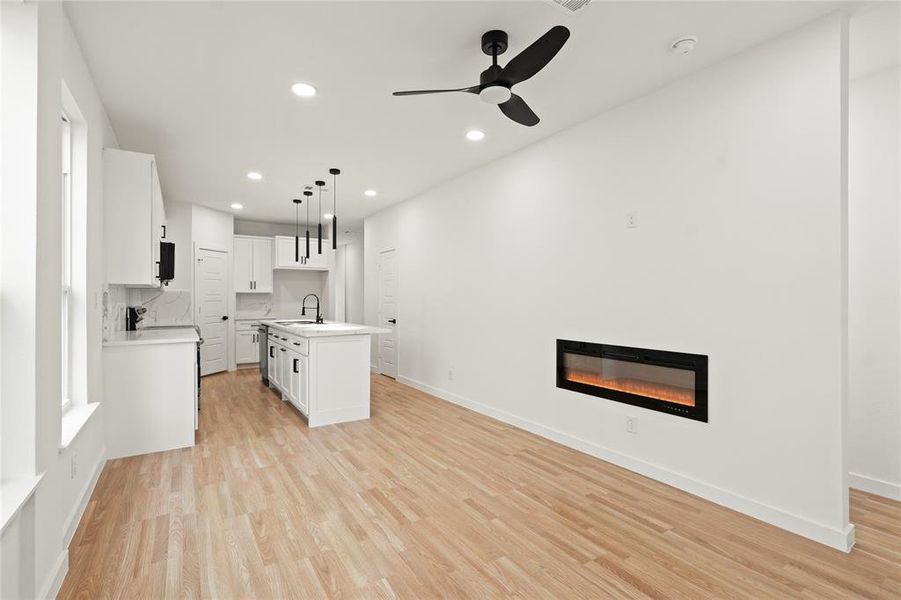 Kitchen with pendant lighting, sink, white cabinetry, a center island with sink, and light wood-type flooring