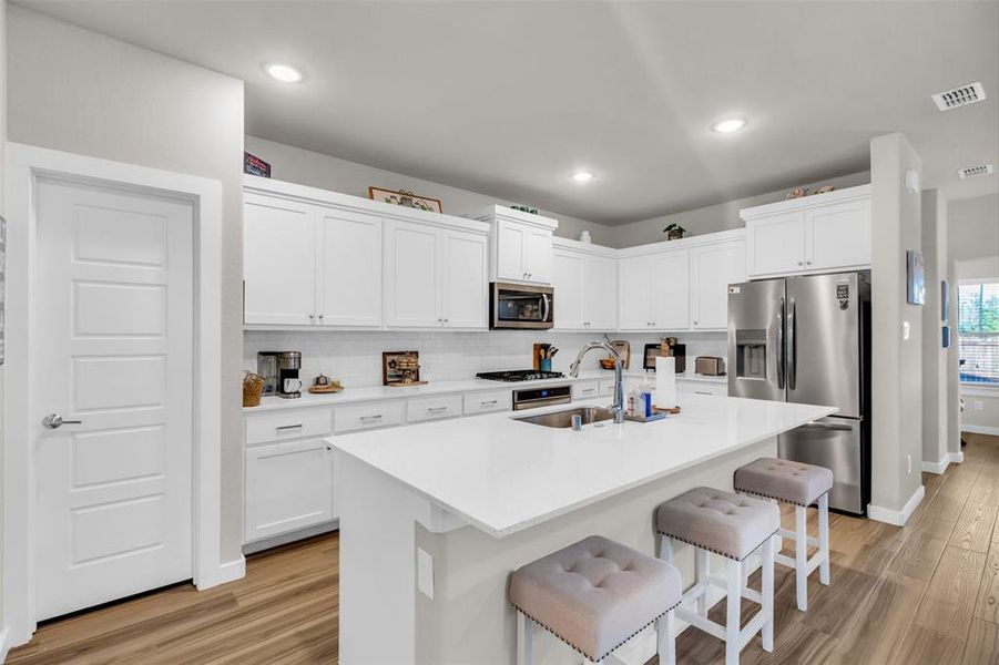 Kitchen with a kitchen bar, white cabinetry, stainless steel appliances, and light hardwood / wood-style flooring