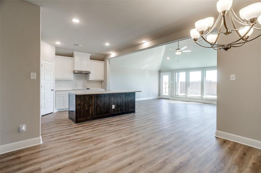 Kitchen featuring vaulted ceiling, a kitchen island with sink, backsplash, white cabinetry, and ceiling fan with notable chandelier Kitchen featuring vaulted ceiling, a kitchen island with sink, backsplash, white cabinetry, and ceiling fan with notable chandelier