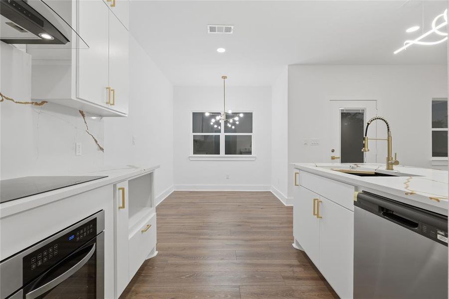 Modern kitchen featuring white cabinetry with gold-tone hardware, wood-finish flooring, built-in stainless steel appliances, and a kitchen island with an integrated sink and gold-tone faucet