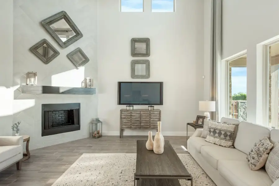 Living room with high ceilings, white fireplace, gray wood floors, and neutral sofa with decorative mirrors on the wall