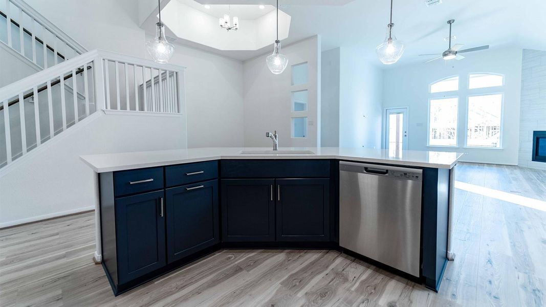 Kitchen with an island with sink, pendant lighting, open floor plan, dishwasher, and light wood-style flooring