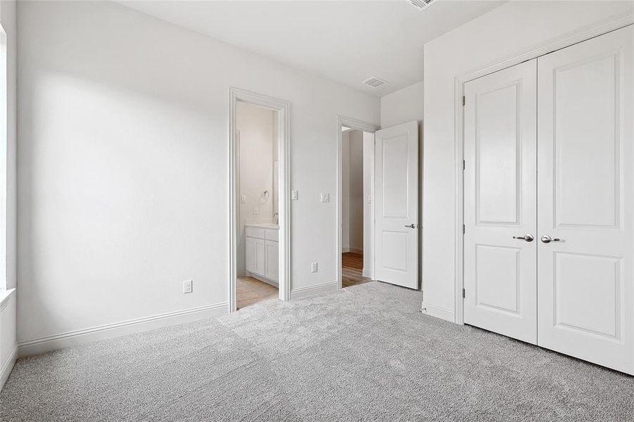 Unfurnished bedroom with light colored carpet, ensuite bathroom, and a closet