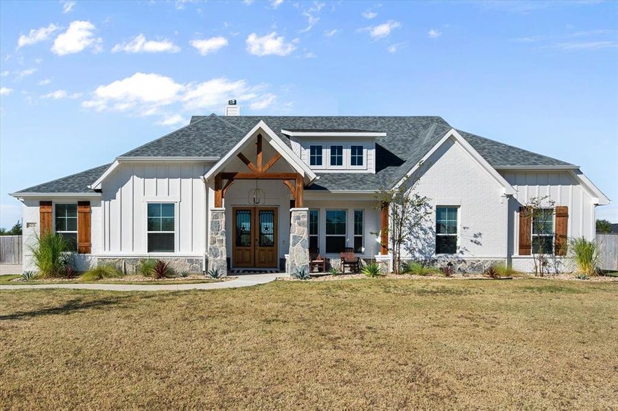Modern farmhouse featuring board and batten siding, a shingled roof, a porch, a chimney, and stone siding