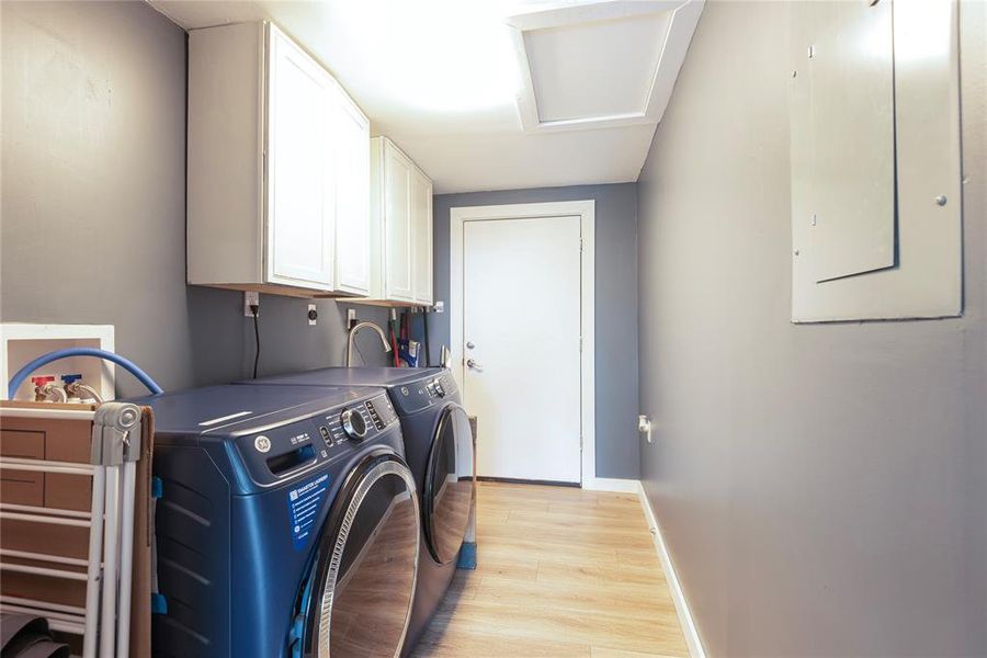 Washroom with light wood finished floors, electric panel, cabinet space, washing machine and clothes dryer, and attic access Washroom with light wood finished floors, electric panel, cabinet space, washing machine and clothes dryer, and attic access