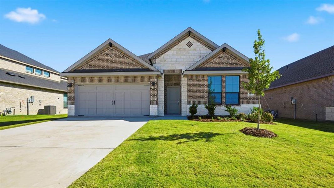 View of front of house featuring brick siding, driveway, a front yard, a garage, and stone siding