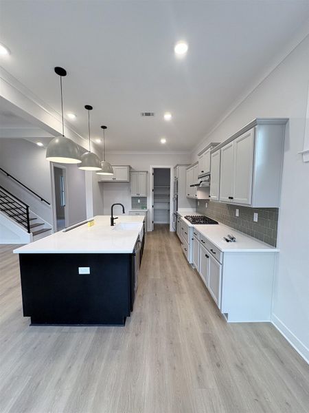 Galley kitchen with a black island, white countertops, and wood-finish flooring Galley kitchen with a black island, white countertops, and wood-finish flooring