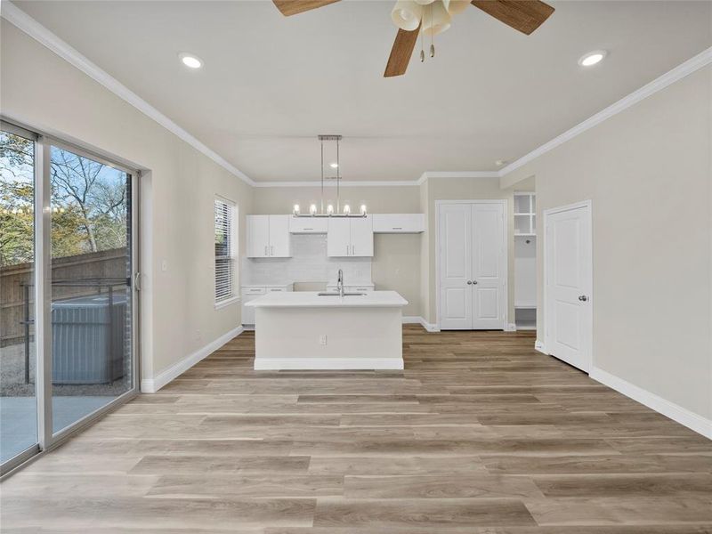 Kitchen featuring crown molding, light wood-style flooring, white cabinetry, a sink, and an island with sink